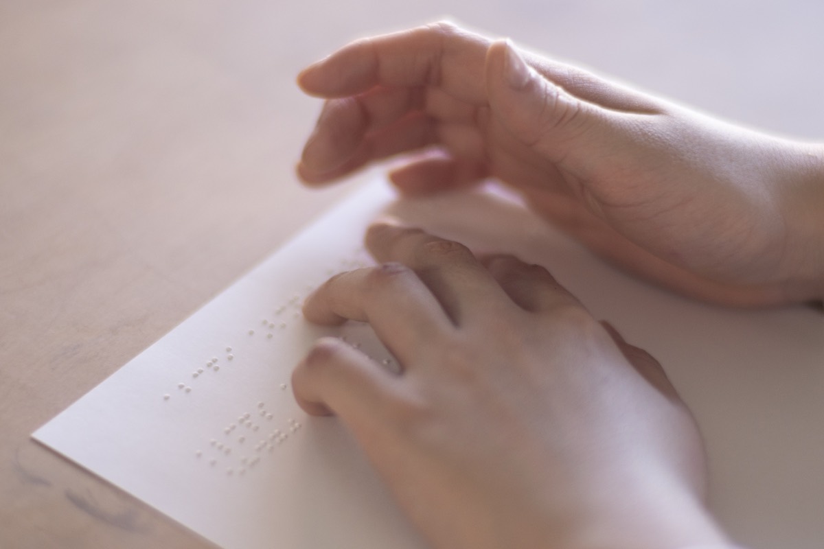 打ち上がった点字の紙面に両手を重ね、指の腹でなぞって読み確かめる手。